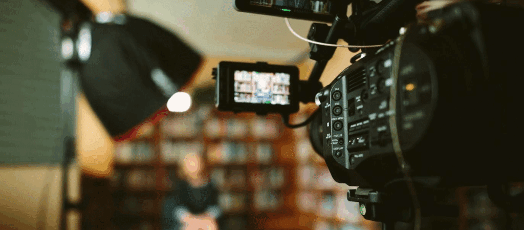 a camera with a viewfinder looks to be filming an interview with a woman in a library