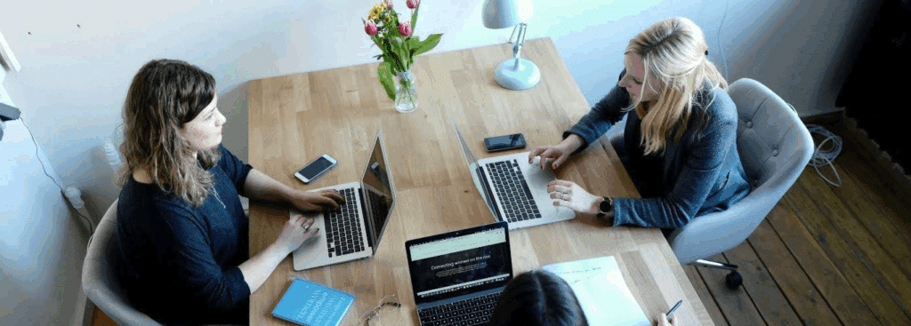Three women sitting around a table working together on laptops.
