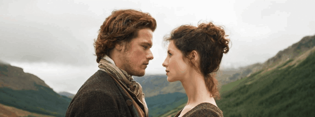 Jamie and Claire staring at each other with the Scottish highlands in the background