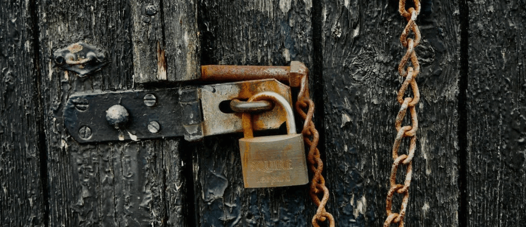 a rusted old padlock on a chain - appears to be locking an old wood door of a barn or something similar.