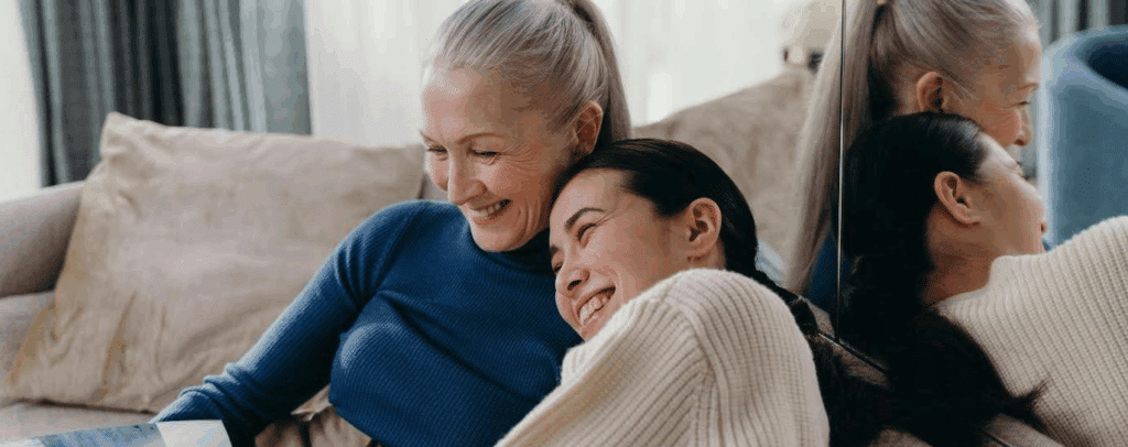 two women laughing together, cuddled up on a couch