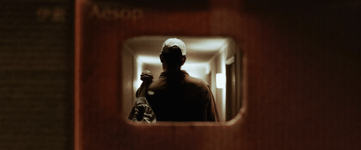 a photo taken from one subway car to another. a man stands in focus through the subway car window.