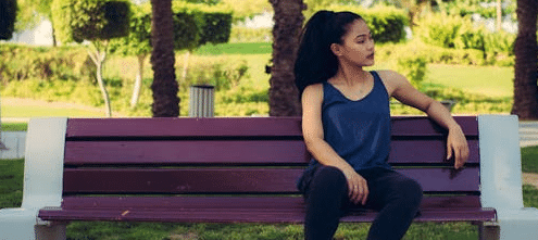 A woman sits on the far end of a park bench, leaving 2/3 of it (and the shot) open - example of rule of thirds