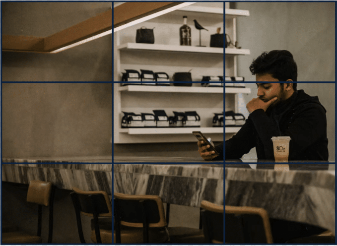 A man sits at a bar, a coffee to his right. He is in the right third of the frame (rule of thirds example)