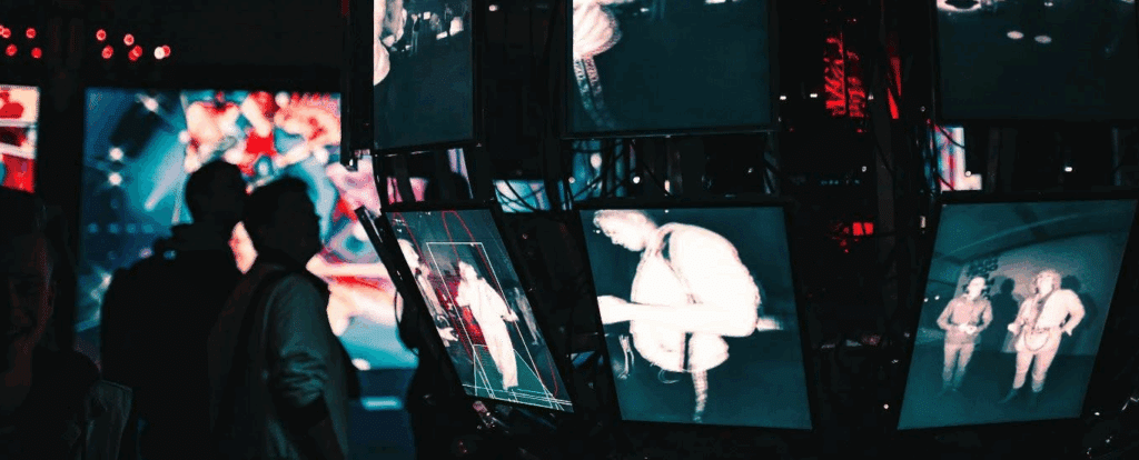 two silhouetted figures stare at a sphere made out of television/computer screens