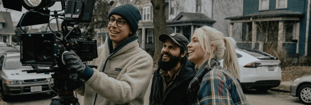 two members of a film crew stand behind a cameraman