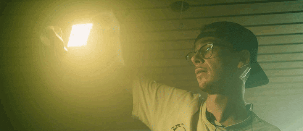 A gaffer holding up a light. He has an earbud in.