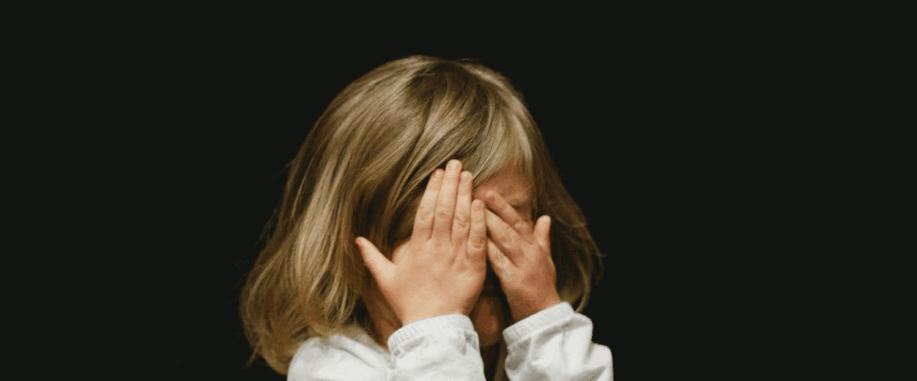 A little girl covers her eyes in fear