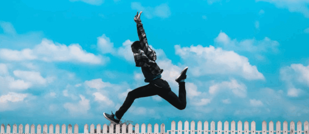 A person leaping in the air with a white picket fence in the background