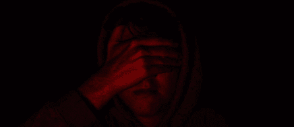 A person in a red light, covering their eyes.