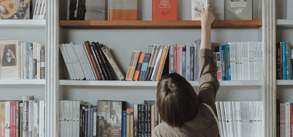 Script opening scene

A woman reaching for a book on an upper shelf of a bookshelf