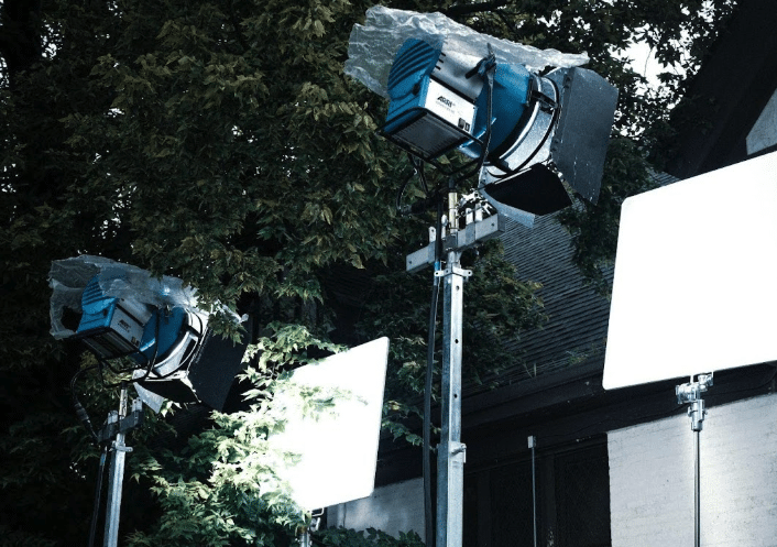 two large spotlights on tall tripods set up pointing at a wall on a film set - part of a gaffer's job.