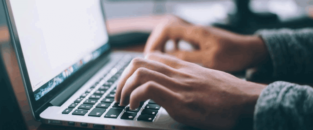 Two hands typing on the keyboard of a laptop