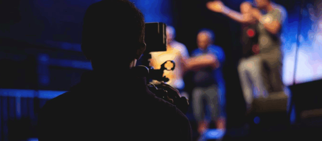 behind the scenes on a film set. the cameraman can be seen in silhouette, the stage/set in the background