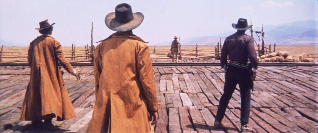 A still from the film Once Upon a Time in the West - three men in hats and coats with their backs to the camera.