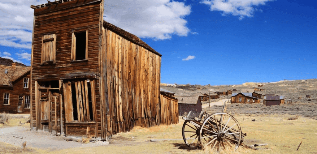 an old wild west town, or ghost town. An old wood building stands in the middle of the desert. An old wooden cart sits beside it.