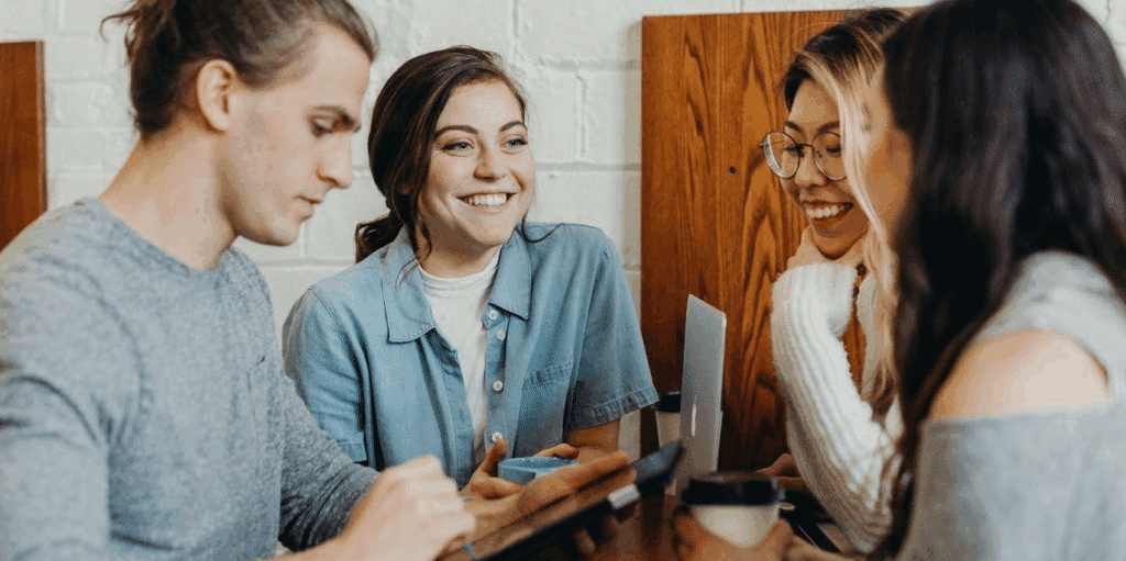 A group of 4 people sitting together at a table and smiling while drinking tea or coffee