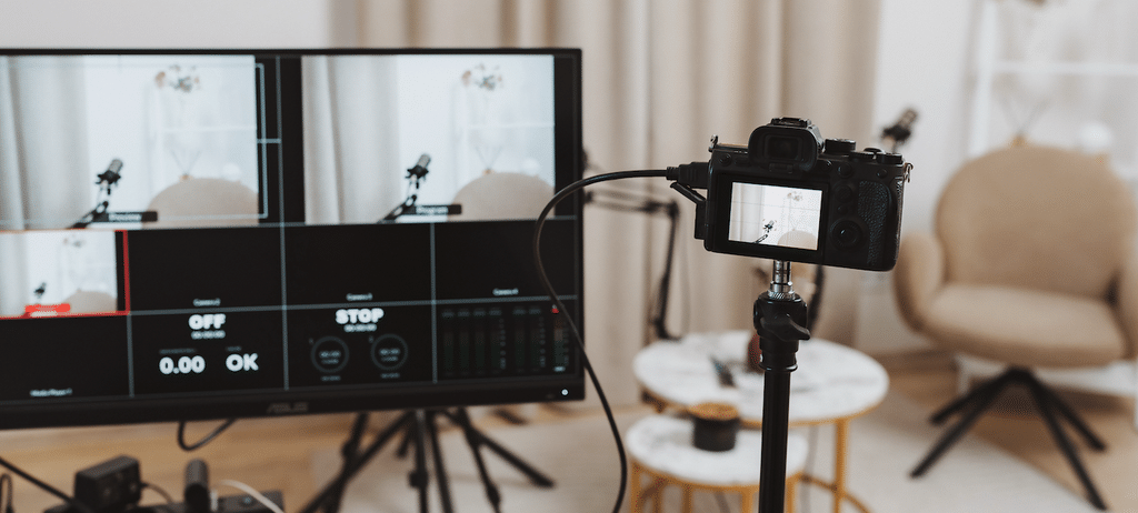 A tripod-mounted camera and monitors showing a locked-off interview setup framed against a window
