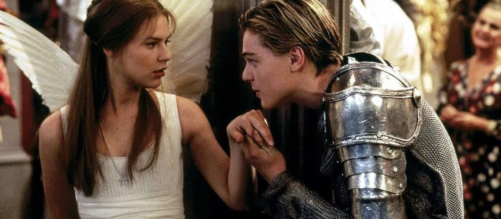 Romeo, in a knight costume, tenderly kisses Juliet's hand while she wears angel wings, at the Capulet party in Baz Luhrmann's Romeo + Juliet (1996)